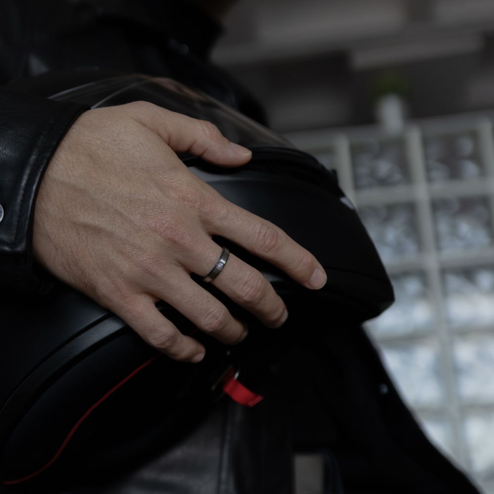 Detalle de anillo con diamantes hombre en zirconio negro gris en mano masculina sobre casco de moto