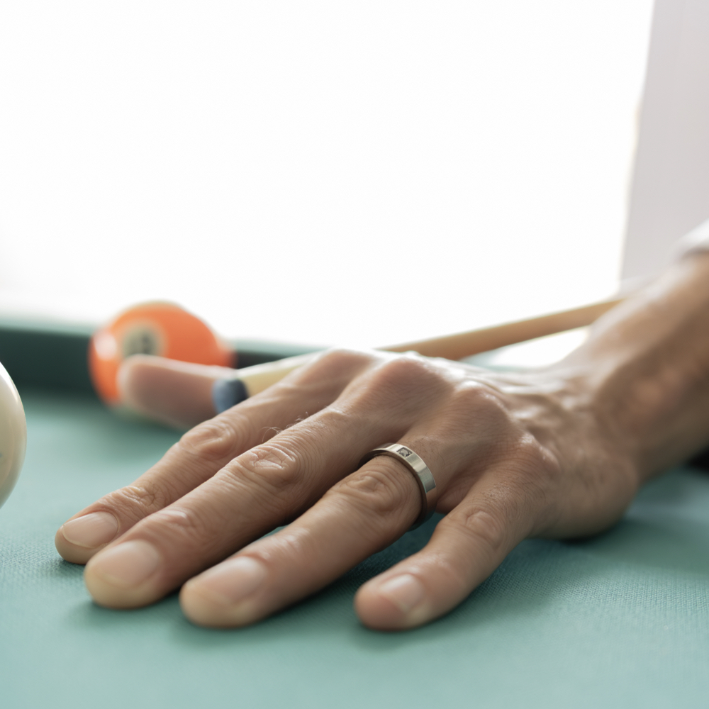 Anillo con piedra hombre en zirconio gris con diamante negro en mano apoyada sobre mesa de billar