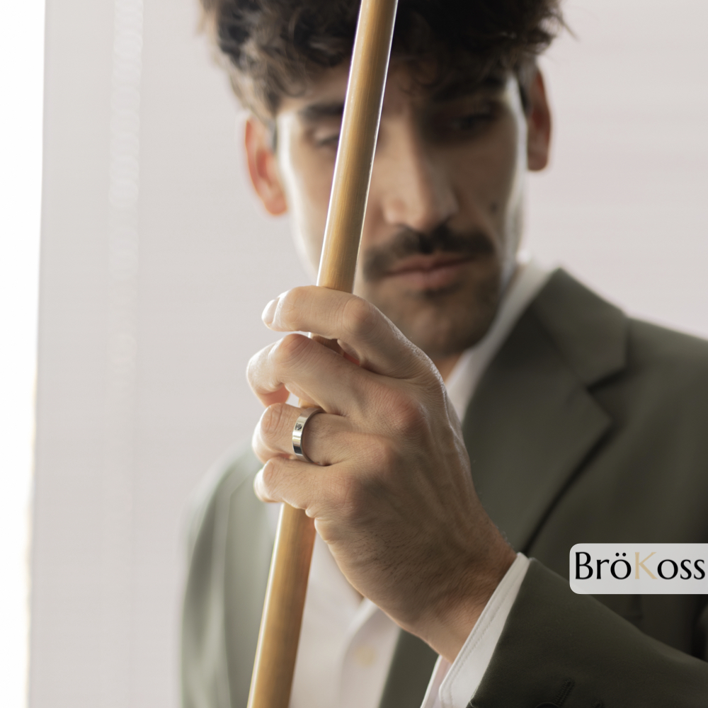 Anillo con piedra negra, modelo posando con palo de billar mientras luce anillo de zirconio gris con diamante negro, estilo elegante y moderno