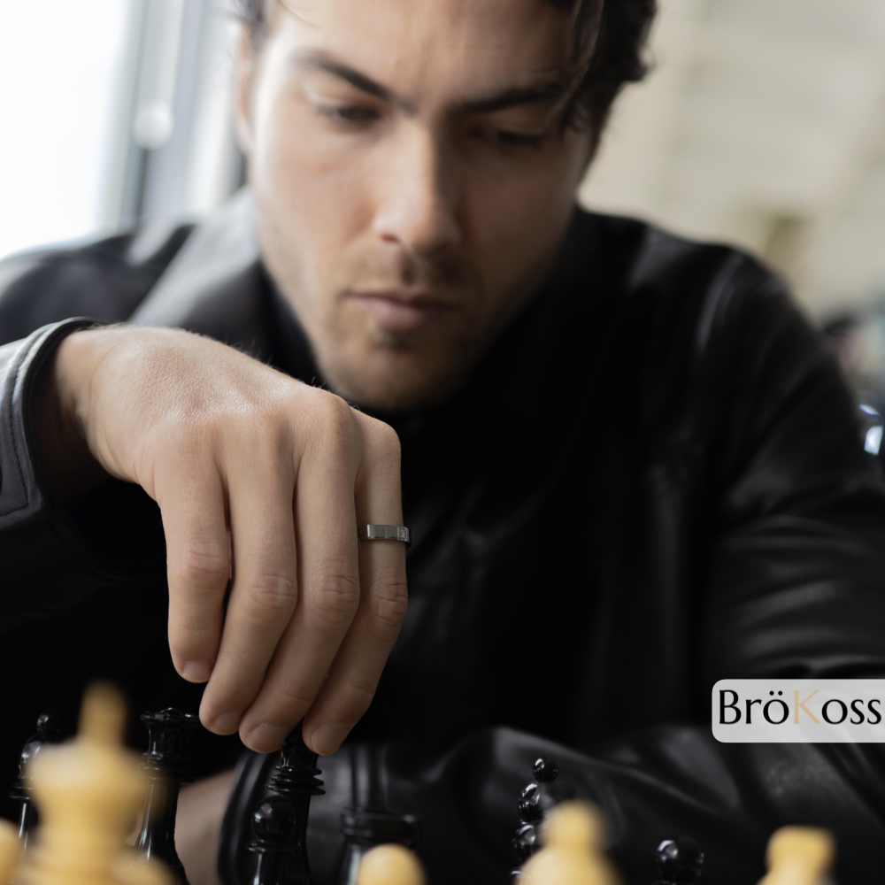 Anillo de diamante para hombre visible en mano mientras juega al ajedrez, estilo elegante