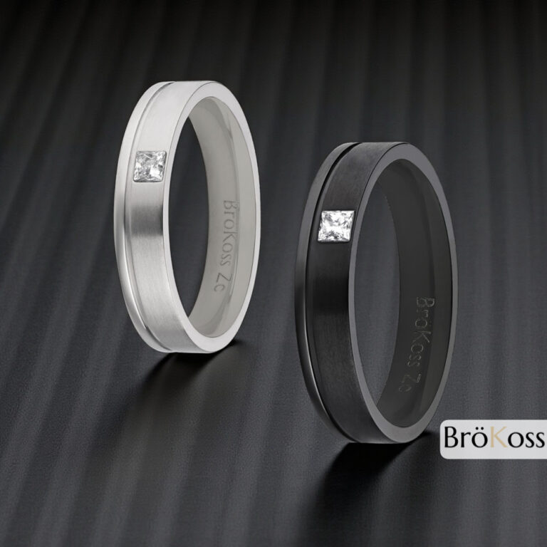 Par de alianzas masculinas estilo oro en zirconio gris y negro, una con diamante cuadrado y otra lisa, sobre fondo de fibra de carbono